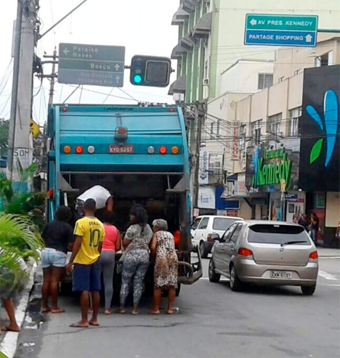 Pessoas remexendo o lixo dentro do caminhão coletor no Centro de São Gonçalo