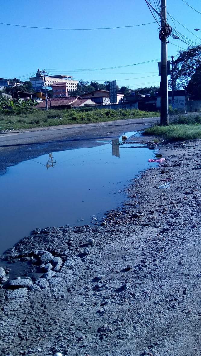 Foto de uma rua no bairro Sacramento, em São Gonçalo, Rio de Janeiro. O chão tem um buraco com água de esgoto, deixando a rua perigosa para pedestres.